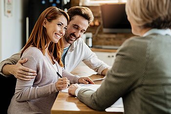 Lächelndes Paar unterzeichnet Mietvertrag mit Unterstützung einer Immobilienexpertin – jetzt möblierte Wohnung stressfrei mit Mr. Lodge in München vermieten.
